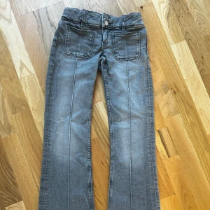 Grå jeans från Gina Tricot - Snygga grå bootcut jeans från Gina Tricot med låg midja. Byxorna har dubbla knappar och framfickor för en stilren look. Perfekta för en avslappnad stil.