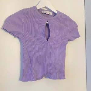 Lila ribbad topp från Bershka - Säljer en söt lila ribbad topp från Bershka med korta ärmar och en liten öppning framtill. Perfekt för en avslappnad stil. 💜