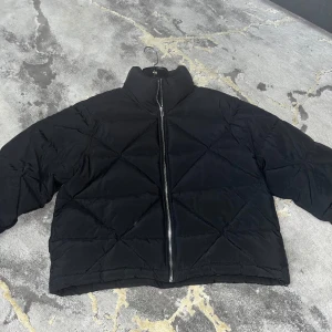 Svart pufferjacka från Gina Tricot - Snygg svart pufferjacka från Gina Tricot med dragkedja framtill. Jackan har en quiltad design och hög krage, perfekt för kyliga dagar. Aldrig använd!!