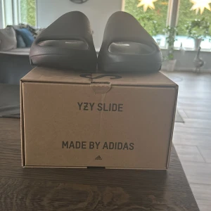 Svarta YZY Slide från Adidas - Säljer ett par svarta YZY Slide från Adidas i storlek 43. Dessa slides är helt oanvända och perfekta till att ha som både inomhus skor eller som ett par sköna tofflor till sommaren! Pris kan diskuteras! Säljaren står för eventuella fraktkostnader.
