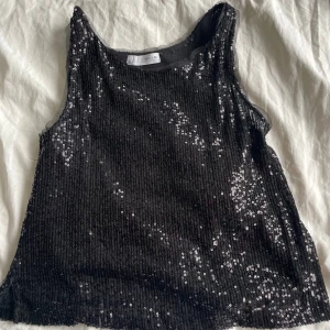 Svart paljettopp från Zara✨ - Snygg svart paljettopp från Zara, perfekt för festliga tillfällen. Toppen är ärmlös och täckt med glittrande paljetter som ger en glamorös look. Passar utmärkt för att sticka ut i mängden.