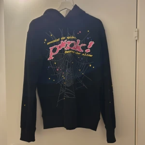 Svart hoodie från Spöuer - Cool svart hoodie från Spöuer med färgglada stjärnor och texten 'never mind the spider, panic! before the slime' på framsidan. Tillverkad i 100% bomull med en avslappnad passform och långa ärmar. Perfekt för en unik stil.