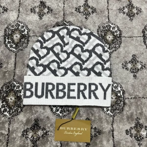 Burberry mössa - Snygg gråvit mössa från Burberry med ett iögonfallande mönster och stor logotyp framtill. Perfekt för att hålla stilen under kallare dagar.