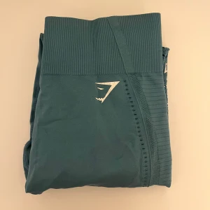 Turkosa leggings från Gymshark - Snygga turkosa leggings från Gymshark med hög midja men som även funkar superbra att vika ner och en tight passform. Perfekta för träning med sitt stretchiga material och stilrena design. Diskret logga på låret. Passar XS-mindre M