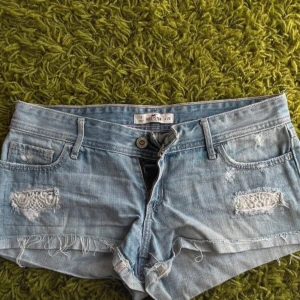Ljusa low rise jeansshorts från Hollister - Säljer ett par ljusa low Rise jeansshorts från Hollister med slitna detaljer och fransig kant. Perfekta för en avslappnad sommarlook. De har en knapp och dragkedja framtill samt klassiska fem fickor.