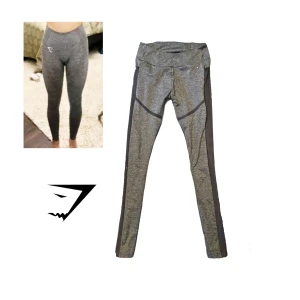 Grå leggings från Gymshark - Snygga grå leggings från Gymshark med svart paneldesign. Perfekta för träning med en tight passform och hög midja. Tillverkade i polyester och elastan för bästa komfort och rörelsefrihet.