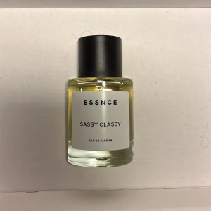 Essnce Sassy Classy Eau de Parfum - Elegant och sofistikerad parfym från Essnce med namnet Sassy Classy. Flaskan är stilren och genomskinlig med en svart kork och vit etikett. Perfekt för den som vill ha en doft som utstrålar både självsäkerhet och klass.