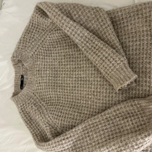 Beige stickad tröja lager 157 - Mysig beige stickad tröja från lager 157. Perfekt för kyliga dagar med sitt varma material och klassiska design. Tröjan har långa ärmar och en rund halsringning. Använd några gånger