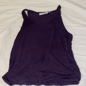 Mörklila linnetopp från Needle  - Snygg mörklila linnetopp från Needle med en liten bröstficka. Perfekt för varma dagar och kan enkelt matchas med olika outfits.