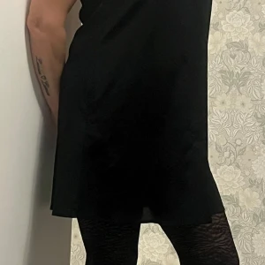 Svart klänning med spetsdetaljer - Elegant svart klänning med vackra spetsdetaljer på axlarna. Klänningen är ärmlös och har en klassisk, tidlös design som passar perfekt för olika tillfällen.