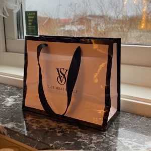 Shoppingväska från Victoria's Secret - Shopping kasse från Victoria's Secret i svart och rosa/beige med deras ikoniska logga. Snyggt till dekoration eller liknande. 