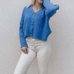 Blå stickad kofta/tröja - Snygg blå kofta med ribbad struktur och stora knappar framtill. Den är croppad och har långa ärmar, perfekt för en avslappnad stil. Passar bra till både jeans och kjol.