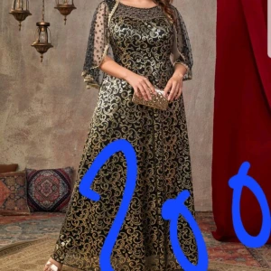 Svart och guld långklänning - Elegant långklänning i svart och guld med glittrigt mönster. Klänningen har trekvartsärmar i transparent material och en rund halsringning. 