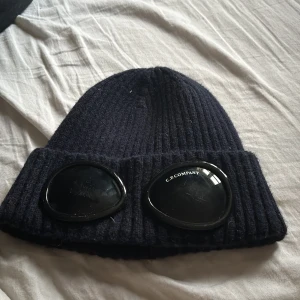 C.p. Company mössa i mörk blå  - Snygg mörkblå ribbad mössa från C.P. Company med unika glasögondetaljer framtill. Perfekt till vinter och få din drip lite fetare pris kan diskuteras bara höra av dig vid frågor😃