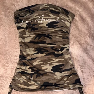 Camouflage tubtopp - Säljer en cool camouflage tubtopp från Shein med glittriga detaljer. Perfekt för en trendig look. Toppen är ärmlös och har ett snyggt mönster i gröna och bruna toner.