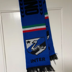 Blå halsduk med Inter Milan - Snygg blå halsduk  Inter Milano och klubbens emblem. Den har ränder i italienska flaggans färger och texten 'INTER' i svart. Perfekt för fotbollsfans!