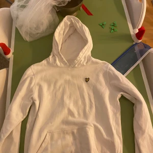 Vit hoodie från Lyle & Scott - Säljer en stilren vit hoodie från Lyle & Scott med deras ikoniska logga på bröstet. Perfekt för en avslappnad look. Den har en klassisk känguruficka och en bekväm huva. 9/10 skick och PRIS DISKUTERAS!
