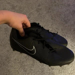Svarta fotbollsskor från Nike - Säljer ett par svarta fotbollsskor från Nike med vit logga. Skorna har snörning och är designade för optimal prestanda på planen.