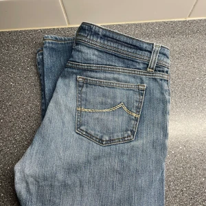 Blå jeans från Jacob Cohen - Säljer ett par snygga blå jeans från Jacob Cohen. De är handgjorda med utvalda japanska tyger och italienskt hantverk. Jeansen har en klassisk femficksdesign och en bekväm passform. Ute för ett dunderpris men är prutbar vid en snabb och smidig affär!