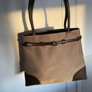 Beige och brun axelväska🥯🤎 - Elegant beige axelväska med bruna detaljer och handtag🤎 Väskan har en stilren design med ett dekorativt bälte framtill. Perfekt för en chic och tidlös look!🙌🏼Både swish och ”köp nu” fungerar utmärkt!❤️