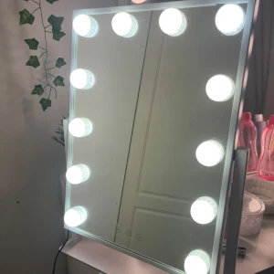 Sminkspegel med LED-belysning - Elegant sminkspegel med inbyggd LED-belysning runt kanterna. Perfekt för att få rätt ljus vid sminkning. Spegeln har en modern design och är utrustad med touch-kontroller för att justera ljusstyrkan. Den är ansluten med en strömkabel på baksidan.