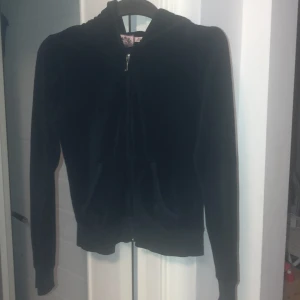 Svart hoodie från Juicy Couture - Säljer en svart hoodie från Juicy Couture med dragkedja och huva. Helsvart rygg. Stl M men mer som xs.