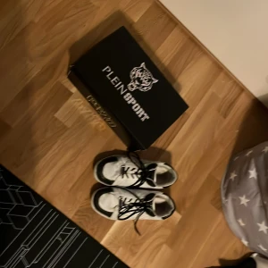 Svartvita sneakers från Plein Sport/Philip Plein sport - Snygga svartvita sneakers från Plein Sport/Philip plein sport med snörning. Perfekta för en sportig look. Skorna har en robust sula och är märkta med storlek 42. Dem är runt 2 och en halv år gammal nya 5 tusen mitt pris 1200 
