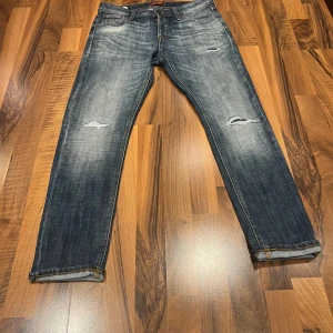 Blå jeans från Jack & Jones - Säljer ett par snygga blå jeans från Jack & Jones, modell Slim/Glenn. De har en slim passform och är tillverkade i denim med slitna detaljer för en trendig look. Perfekta för en avslappnad stil.