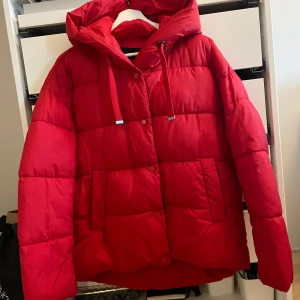 Röd pufferjacka från Vero Moda - Säljer en snygg röd pufferjacka från Vero Moda. Jackan har en mysig huva och stängs med både dragkedja och knappar. Perfekt för kyliga dagar!