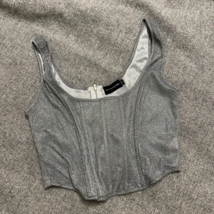 Glittrig silver korsett från PrettyLittleThing - Snygg glittrig silver korsett från PrettyLittleThing med dragkedja i ryggen. Perfekt för en festlig look.