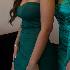 Grön balklänning - Elegant grön axelbandslös klänning med en smickrande passform och slits. Perfekt för speciella tillfällen. ENDAST ANVÄND EN GÅNG, pris KAN DISKUTERAS. 