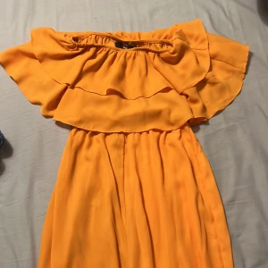 Slutsåld byxdress från bikbok med volangdetaljer - Snygg gulorange byxdress i storlek xs med volangdetaljer och offshoulder-design. Helt slutsåld överallt. Perfekt för event eller sommarevenemang. Klänningen har en luftig passform och är tillverkad i ett lätt material. Endast använd under ett event (bild 2)