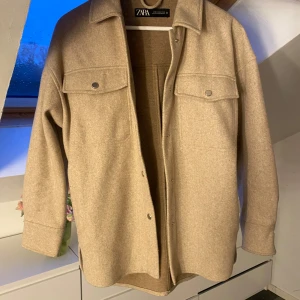Beige overshirt från Zara - Snygg beige overshirt från Zara med knappar framtill och två bröstfickor. Perfekt för lager-på-lager-stil. Den har långa ärmar och en klassisk krage.