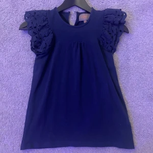 Mörkblå topp med spetsdetaljer - !Storlek känns större! Snygg mörkblå topp med spetsdetaljer på ärmarna. Perfekt för en stilren look. Toppen har en rund halsringning och korta ärmar med vackra spetsdetaljer.💙