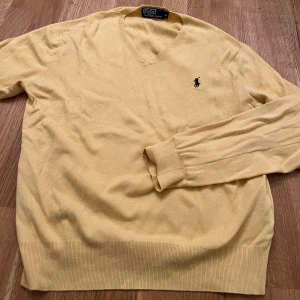 Gul tröja från Polo Ralph Lauren - Säljer en stilren gul tröja från Polo Ralph Lauren med v-ringning och broderad logga på bröstet. Tröjan har långa ärmar och är tillverkad i ett mjukt material som passar perfekt för både vår och höst.