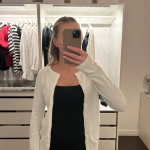 Vit kofta med knappar - Säljer en stilren vit kofta med knappar framtill. Perfekt för lager-på-lager och passar till många olika outfits. Koftan har långa ärmar och en klassisk design. Använd några gånger men i okej skick 