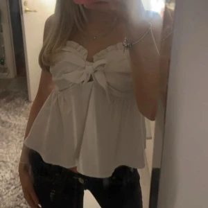 Vit axelbandslös topp med rosett - Säljer en söt vit axelbandslös topp med en liten rosett framtill. Toppen är perfekt för varma dagar. Passar bra till både jeans och kjol.