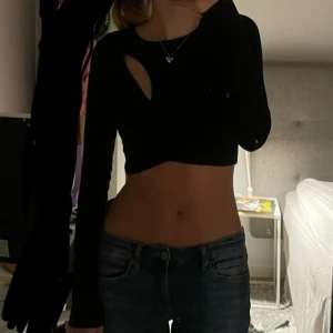 Svart långärmad croppad nyårstopp - Snygg svart långärmad topp med unik cut-out detalj. Den är croppad och har en tight passform, perfekt för en trendig look. Passar bra till både jeans och kjol.