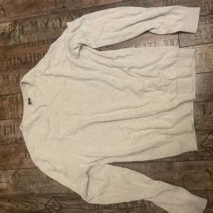 Vit stickad tröja - Säljer en klassisk vit stickad tröja med v-ringad hals. Tröjan har långa ärmar och ribbade muddar vid ärmslut och nederkant. Perfekt för kyligare dagar.