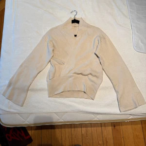 Ribbad tröja - Säljer en stilren beige ribbad tröja med omlott-design. Tröjan har långa ärmar och en bekväm passform. Aldrig använd!