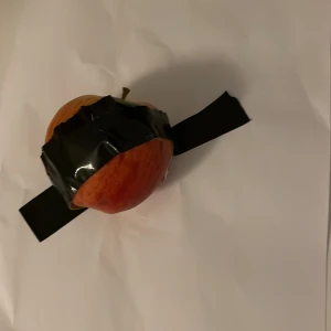 Gjort av Leonardo da Vinci - Ett äpple fasttejpat på ett papper med svart tejp. Äpplet är rött och tejpen är bred och svart, vilket ger en kontrast mot det vita pappret.