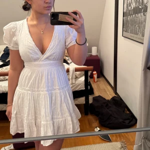 Zara klänning - Söt vit omlottklänning med korta ärmar och volangdetaljer. Perfekt för sommarens varma dagar. Klänningen har en v-ringad design och en luftig passform. Perfekt för student 