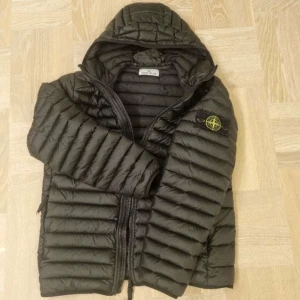 Svart dunjacka från Stone Island - Snygg svart dunjacka från Stone Island med huva och dragkedja. Jackan är i storlek S och passar "true to size". Jackan är i nyskick och tillkommer med orderbekräftelse och kvitto från Miinto. Nypris 8000kr. Skriv om ni har minsta frågor eller funderingar!.