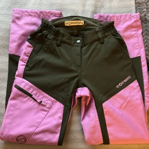 Friluftsbyxor från Stormberg - Snygga och funktionella friluftsbyxor från Stormberg i en cool kombination av rosa och svart. Byxorna har flera praktiska fickor med dragkedjor och elastisk midja för extra komfort. Perfekta för utomhusaktiviteter! 