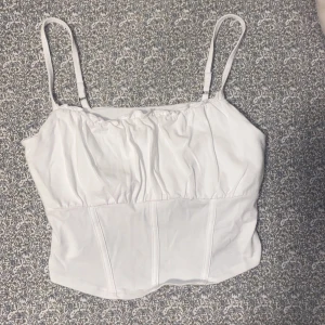 Vit korsettopp från Hollister - Säljer en stilren vit korsettopp från Hollister med justerbara axelband. Jag har knappt använt den då den är för stor på mig 🤍🎀