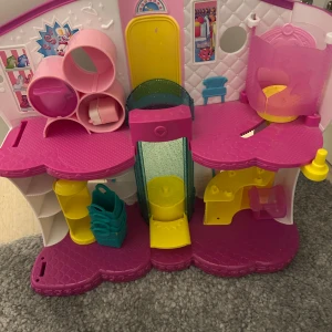 Chopkins hus - Säljer ett färgglatt dockhus med flera våningar och lekfulla detaljer. Huset har rosa, gula och blå inslag med olika rum och tillbehör. Perfekt för kreativa lekar och fantasifulla äventyr.