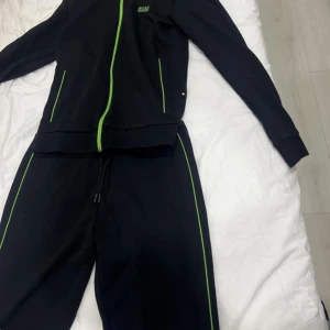 HUGO BOSS SUIT - Snygg svart träningsdräkt från Boss med gröna detaljer. Setet består av en jacka med dragkedja och matchande byxor. Perfekt för en sportig look eller avslappnad dag. STORLEK: M på byxor och S på koftan (båda ingår)