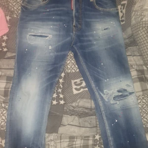 Blå jeans från Dsquared2 - Snygga blå jeans från Dsquared2 med slitna detaljer och färgstänk. De har en klassisk femficksdesign och en dragkedja. Perfekta för en avslappnad stil.