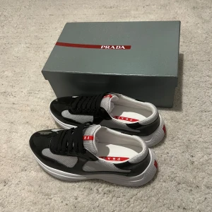 Svart och vit sneaker från Prada - Snygga sneakers från Prada i svart och vitt med röda detaljer. Skorna har en modern design med snörning och en bekväm sula. Perfekta för en stilren look.