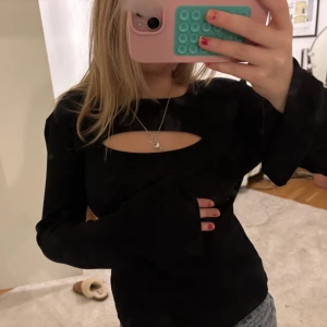 Svart långärmad topp med cut-out - Snygg svart långärmad topp med en trendig cut-out detalj vid bröstet. Perfekt för en stilren look. Passar bra till både jeans och kjol.